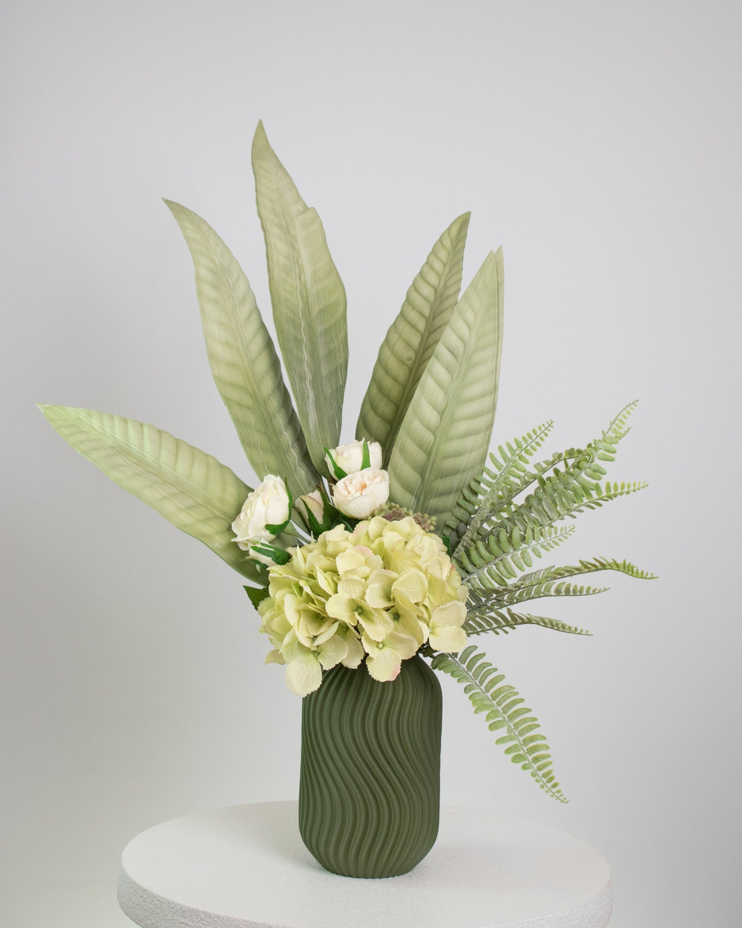 Green blooms arranged in a modern, matte olive vase with gentle wave textures