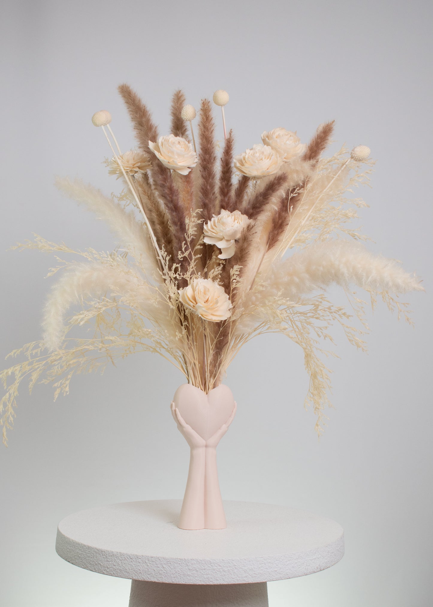 Dried floral arrangement with pampas grass and preserved flowers in neutral tones, displayed in a heart-in-hand vase