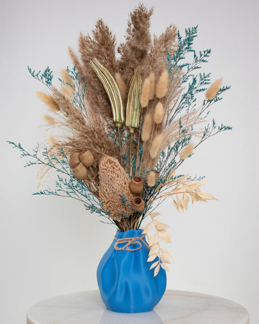 Decorative dried plant arrangement in a blue vase on a white pedestal