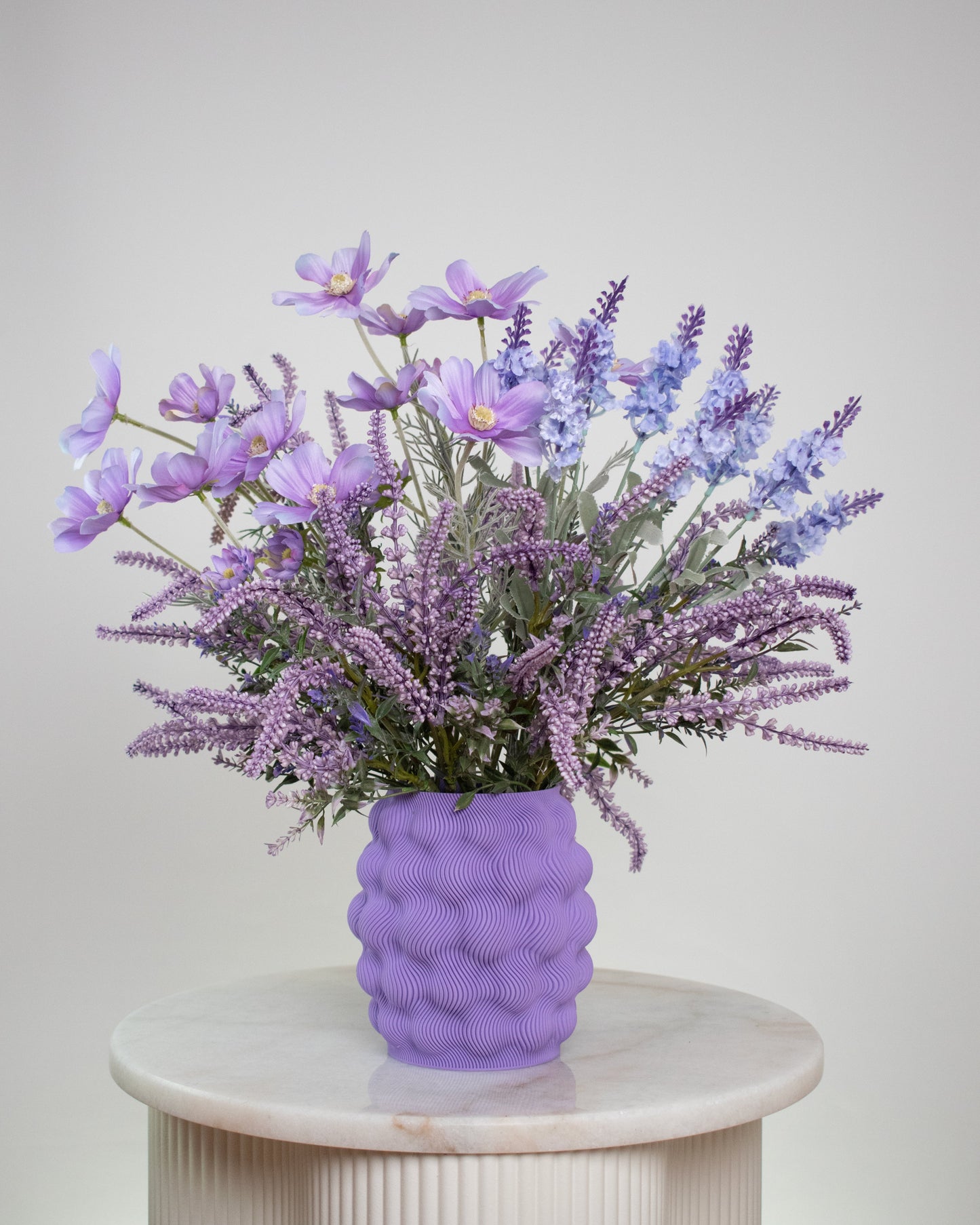 Purple textured vase with a bouquet of purple flowers on a white pedestal against a light gray background
