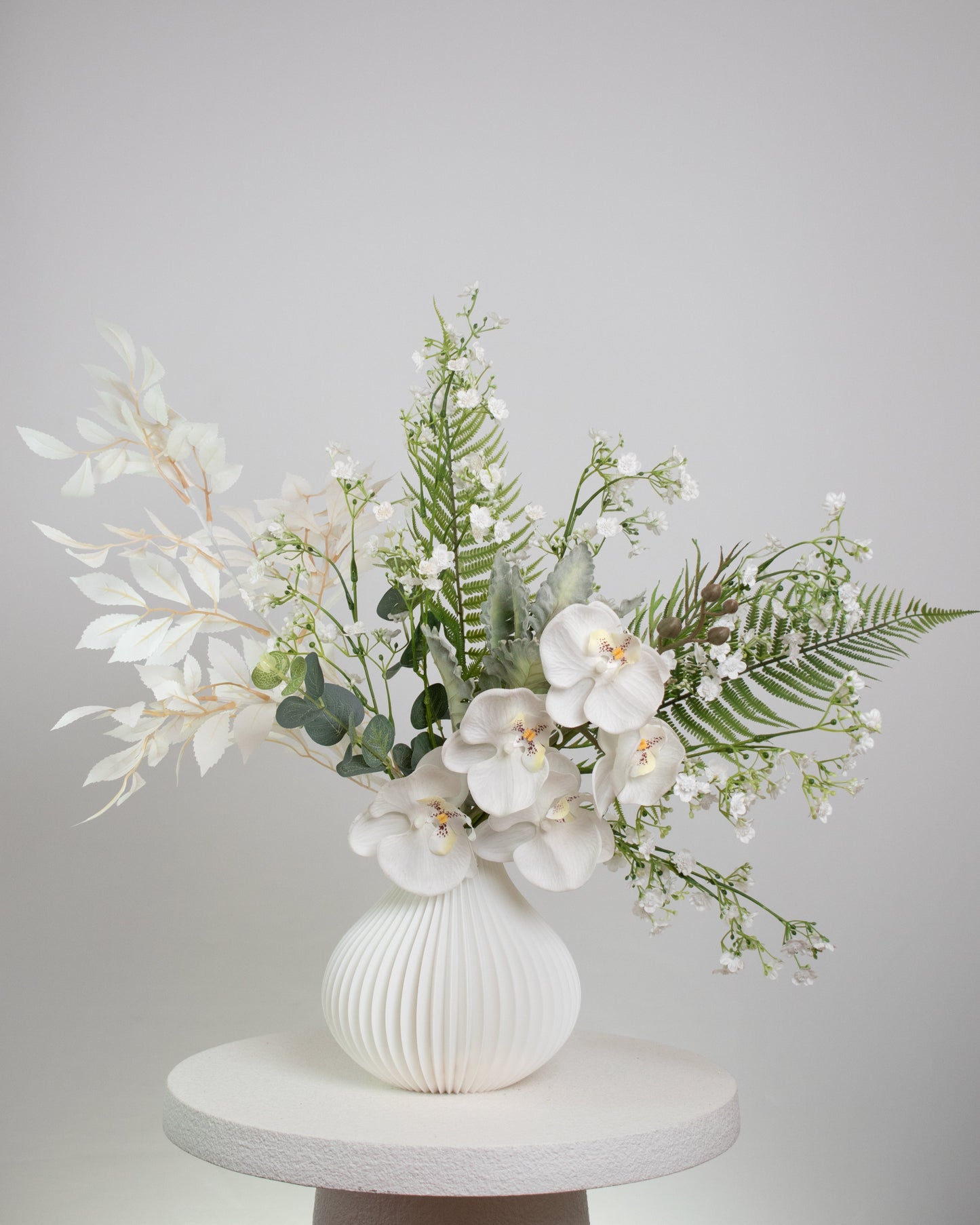 White orchid and foliage artificial flower display in sculpted white vase, minimalist interior décor.