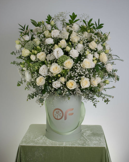 One-metre tall luxury white rose and lisianthus flower arrangement in a branded round box with greenery and baby's breath.
