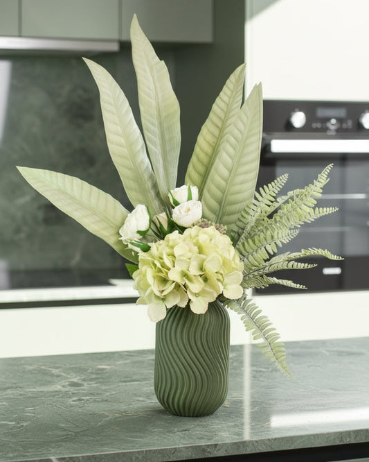 Green vase with flowers and leaves on a white surface against a light gray background