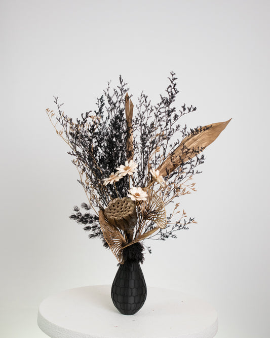 Black textured vase with dried flowers on a white and gold pedestal 