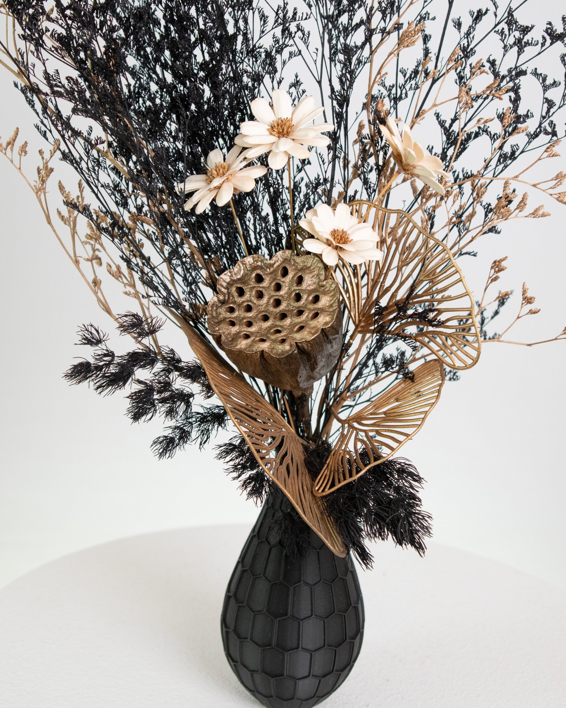 Decorative arrangement of dried flowers and leaves in a black vase 