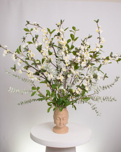 Elegant artificial floral arrangement with white blossoms and green leaves arranged in a beige Buddha head vase, symbolizing calmness and balance in modern décor.