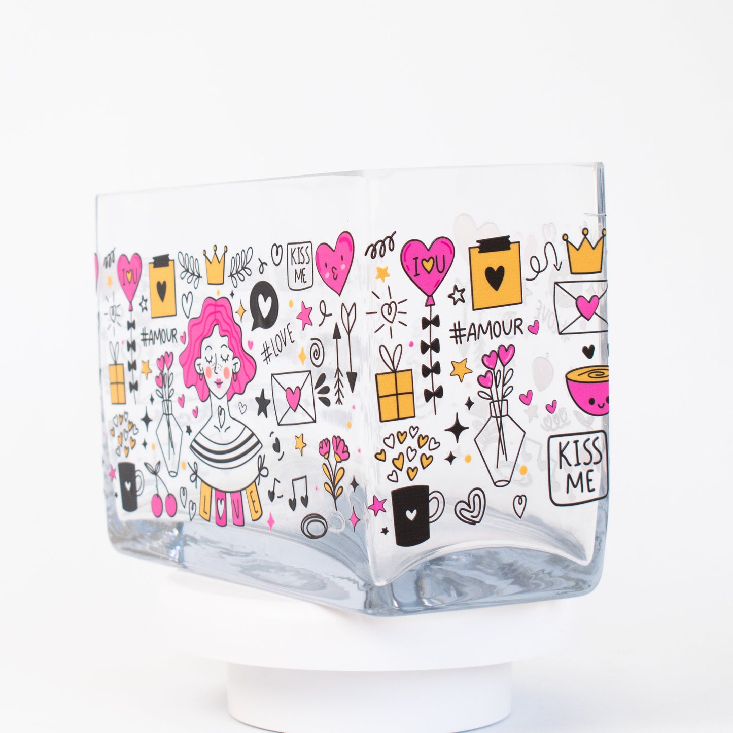 A clear rectangular glass vase featuring a colourful illustrated design of a pink-haired woman surrounded by hearts, flowers, love letters, and doodles in pink, gold, and black tones.