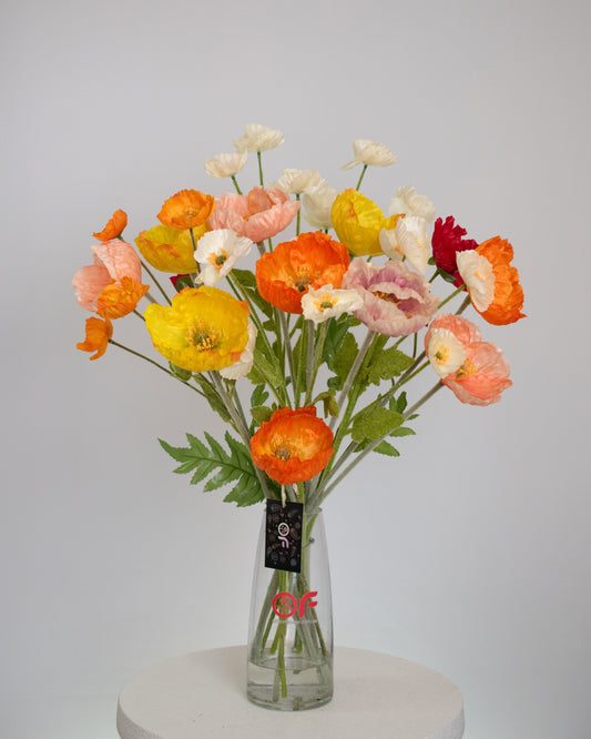 Artificial poppy-style floral arrangement with orange, yellow, pink, and white flowers, arranged in a clear glass vase with acrylic water