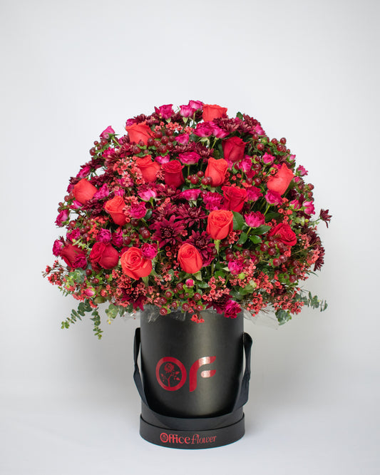 Red rose arrangement in a black gift box with red fillers and black ribbon handles