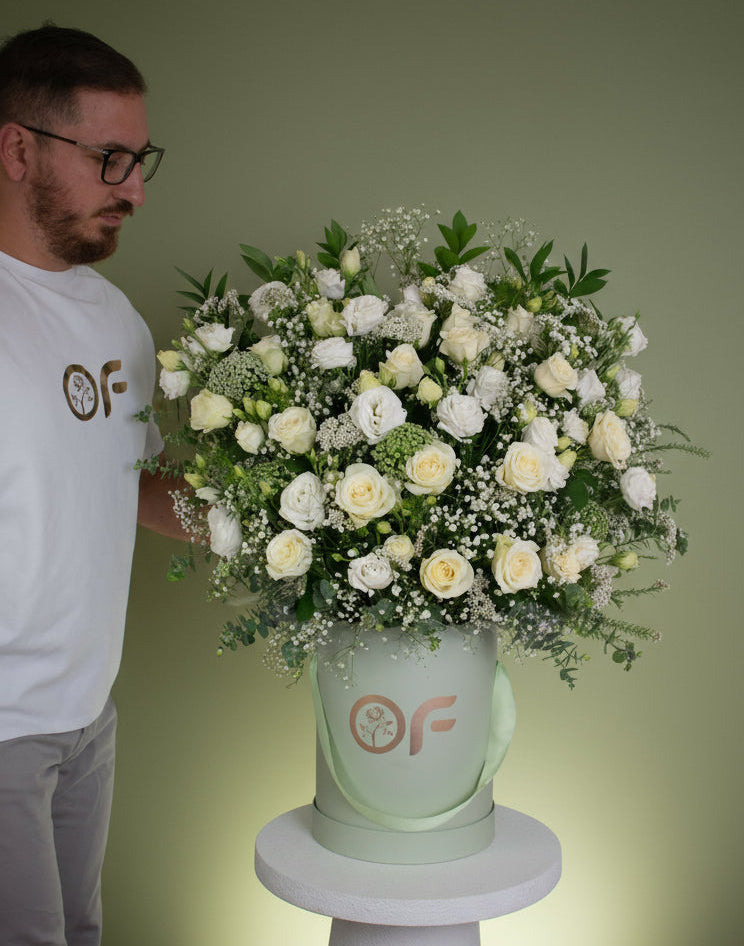 One-metre tall luxury white rose and lisianthus flower arrangement in a branded round box with greenery and baby's breath.